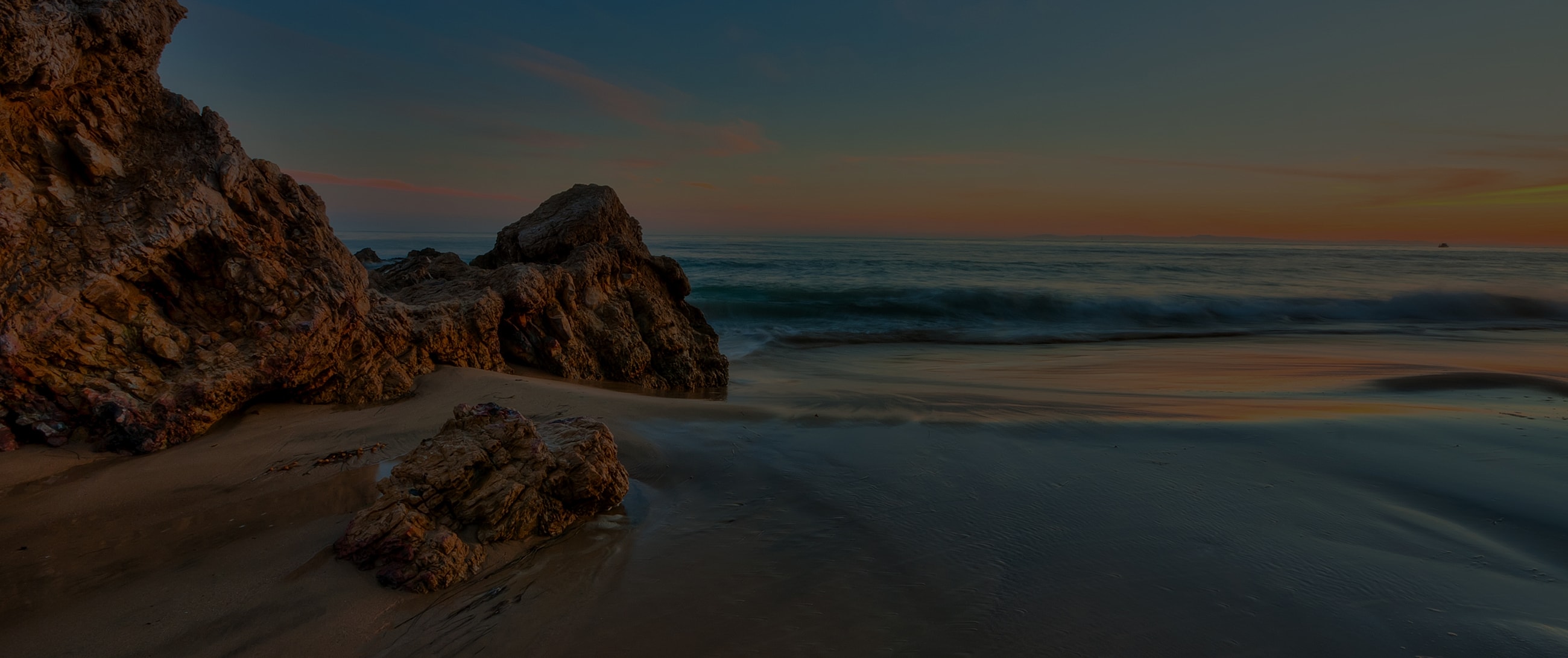 Beach at sunset with rocky shoreline.
