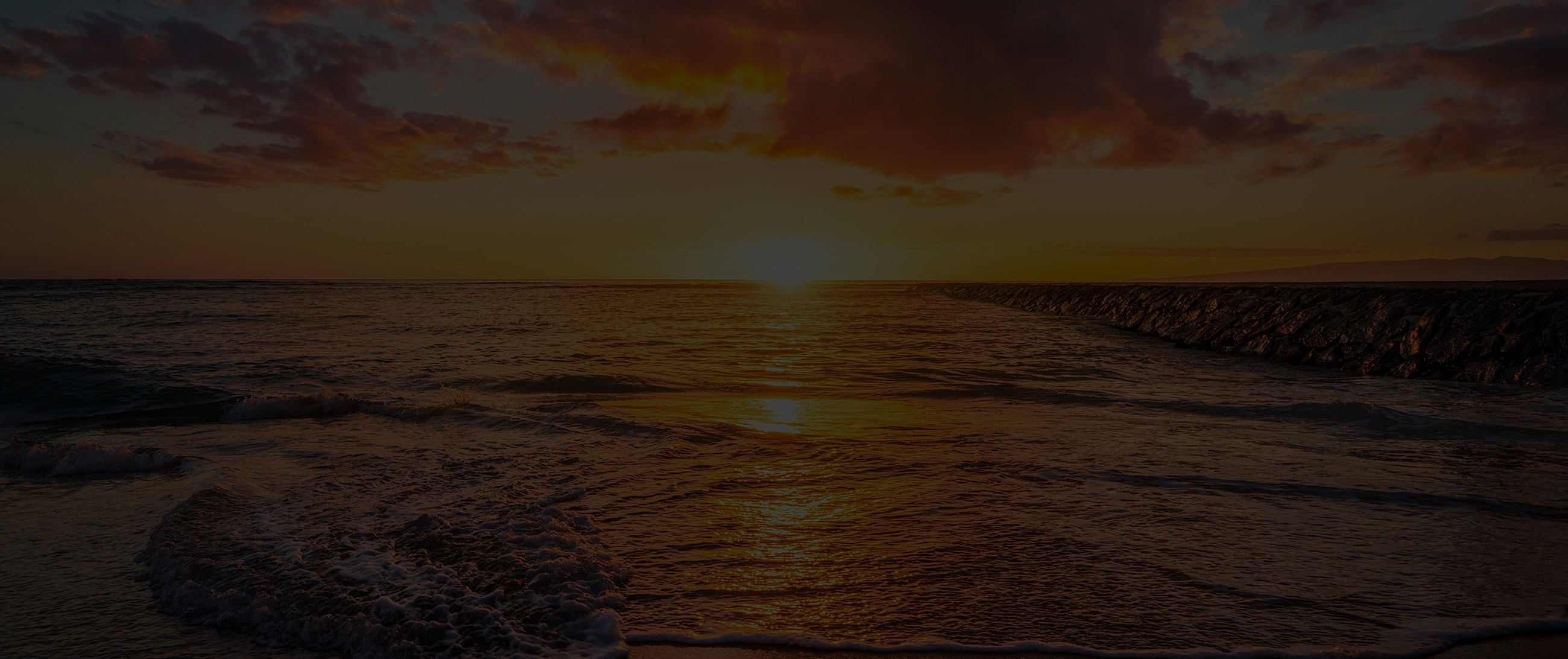 Sunset over ocean with clouds and shoreline.