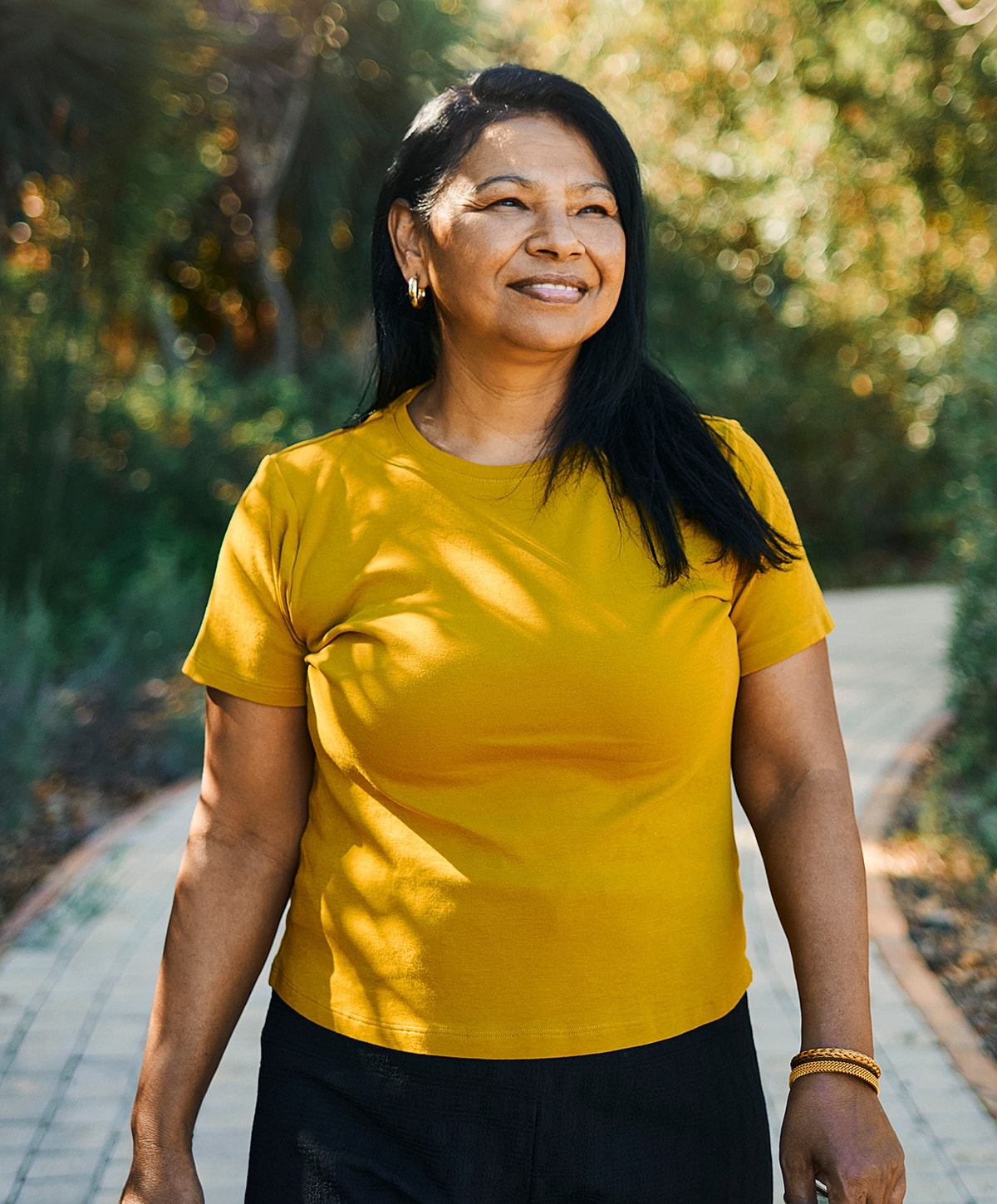 Smiling woman wearing a yellow shirt outdoors.