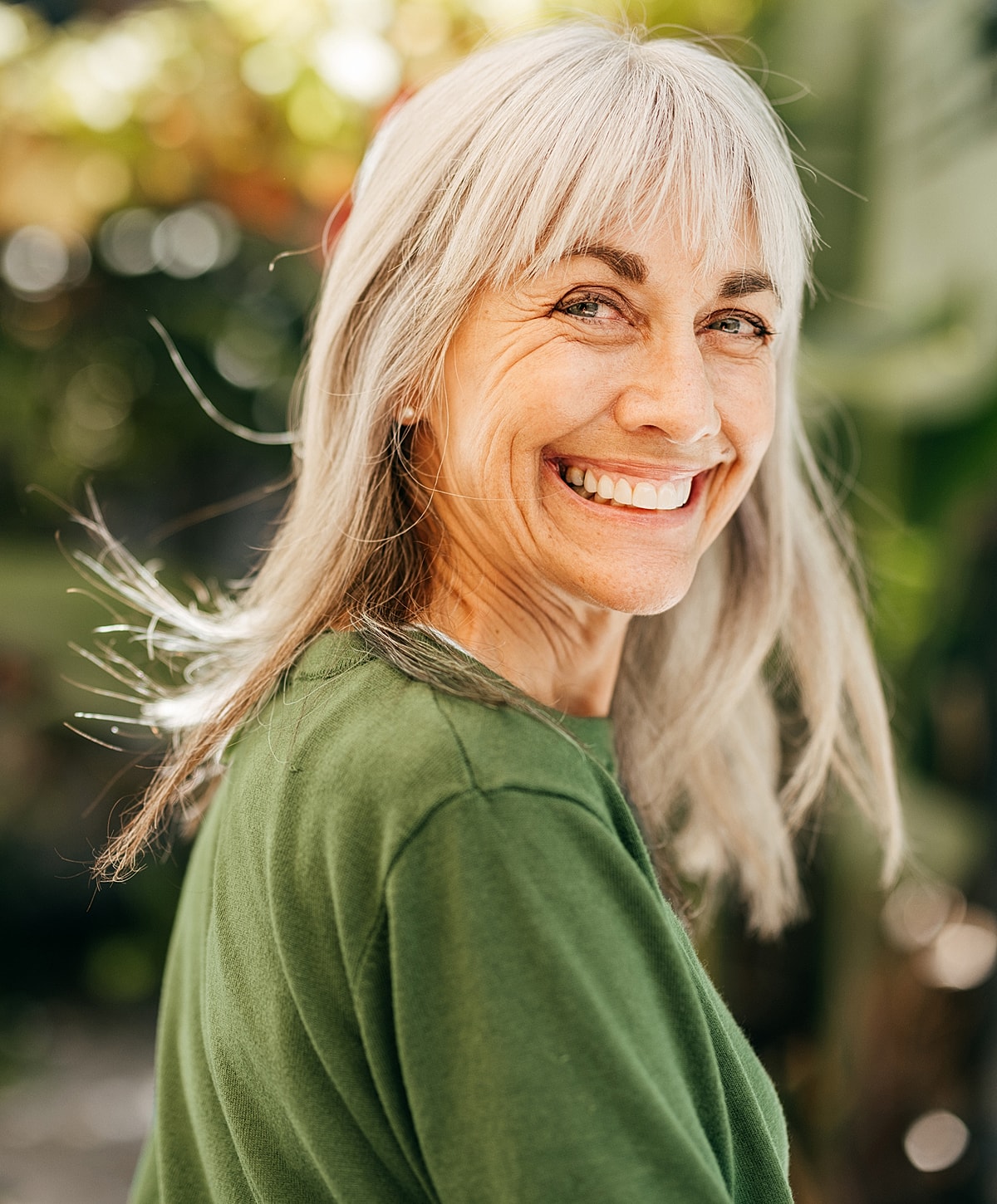 Smiling woman with long gray hair outdoors.