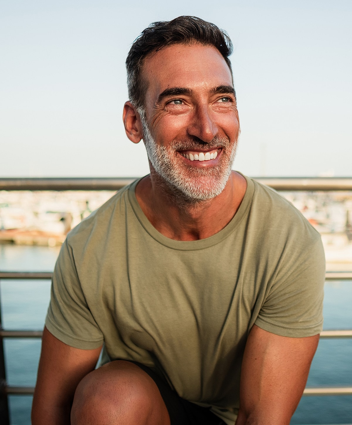 Smiling man by water in casual attire.