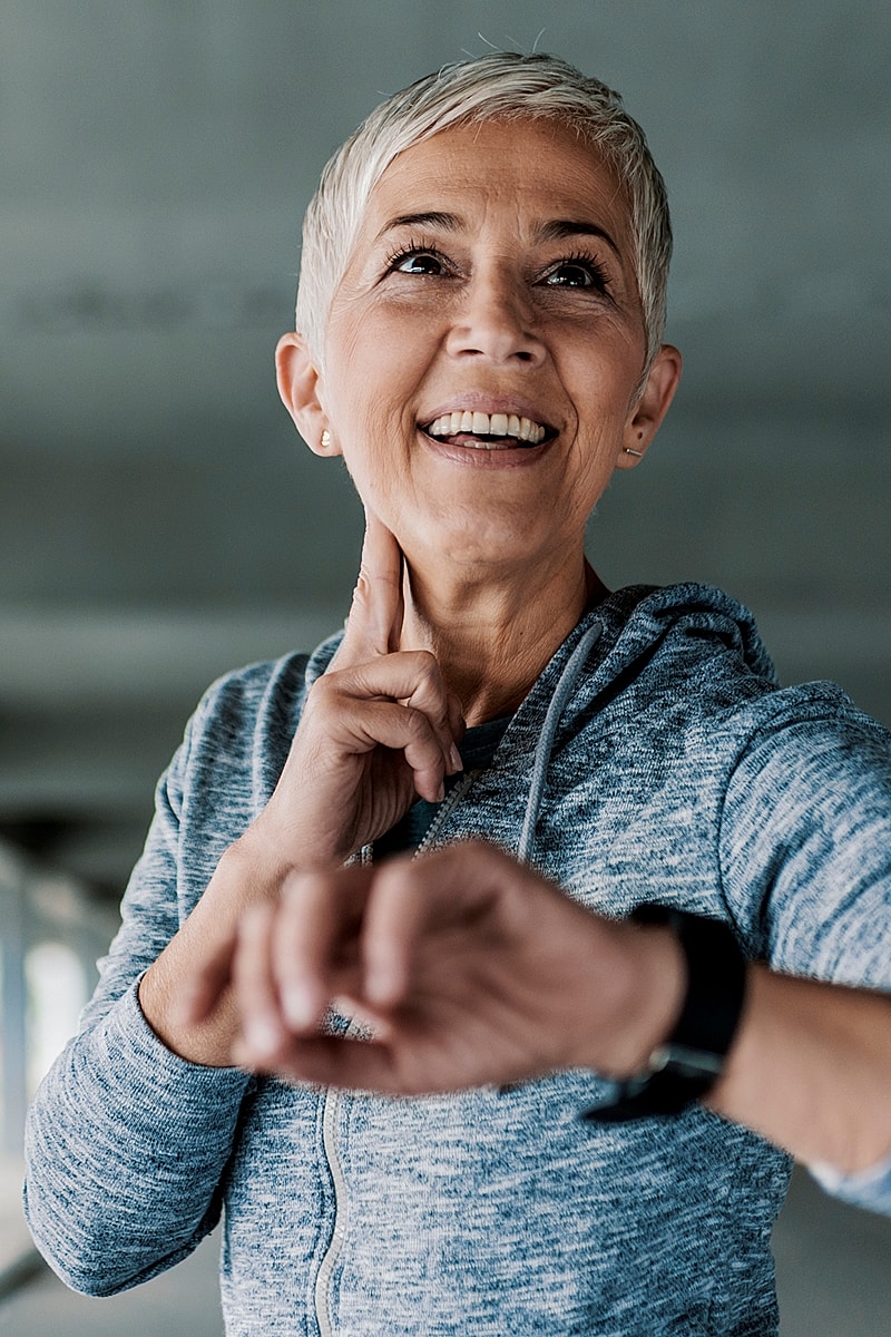 Smiling older woman checking her watch indoors.