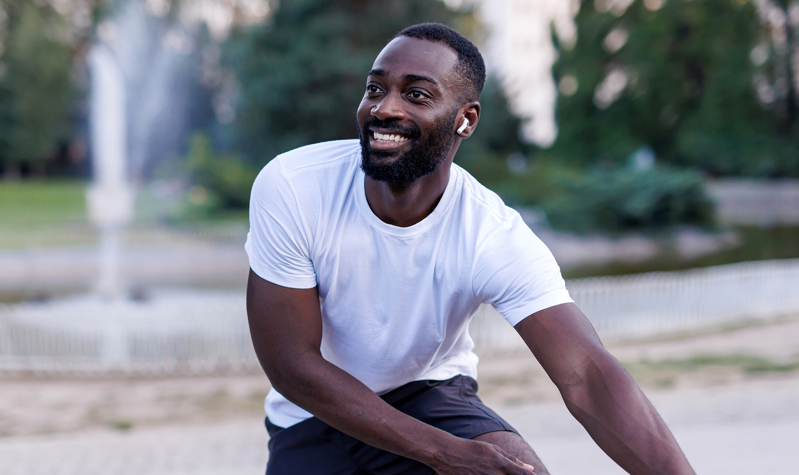 Smiling man exercising outdoors with wireless earbuds.