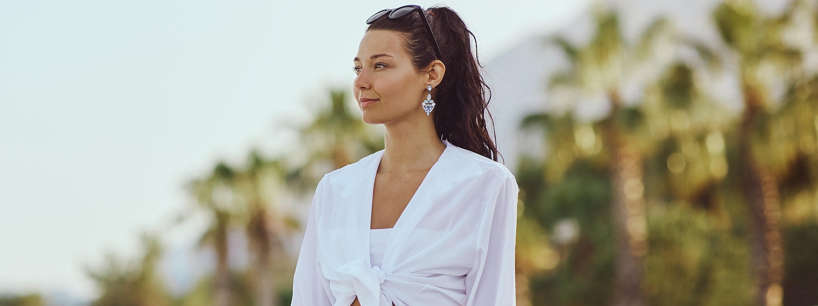 Woman in white outfit against palm trees backdrop.