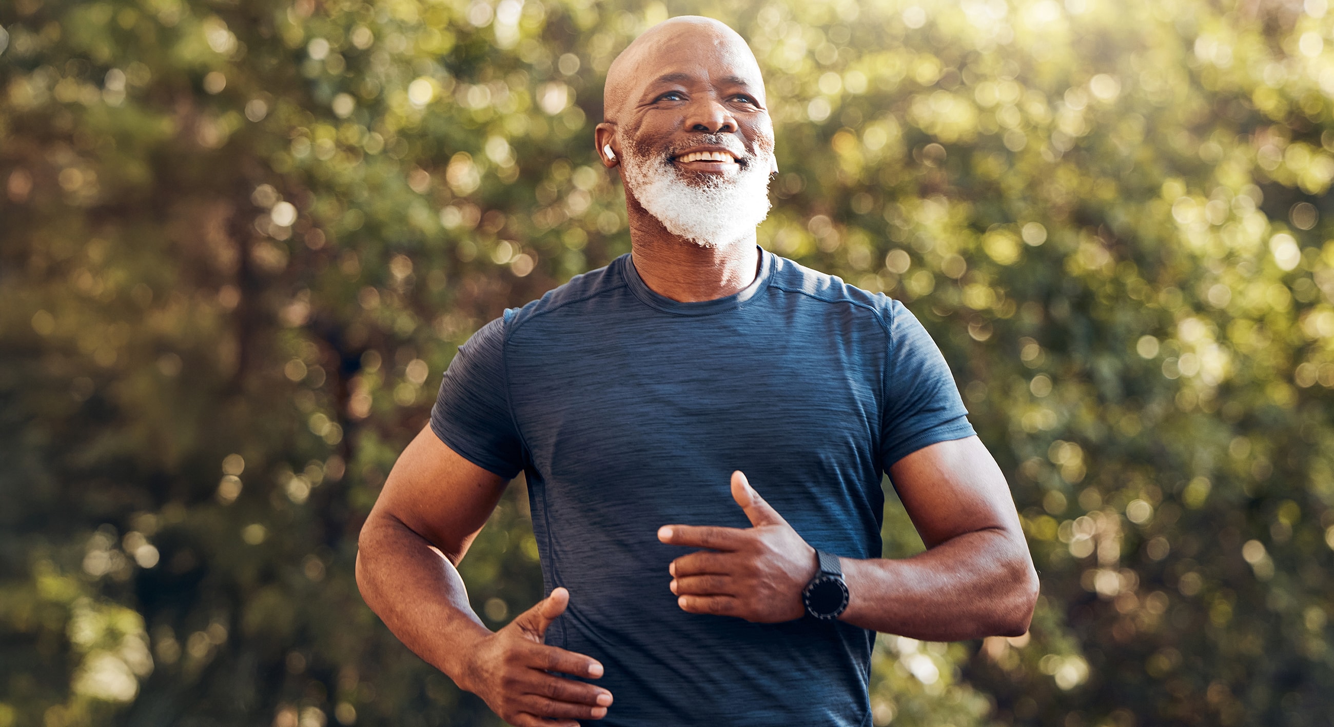 Older man jogging outdoors, smiling in sunlight.