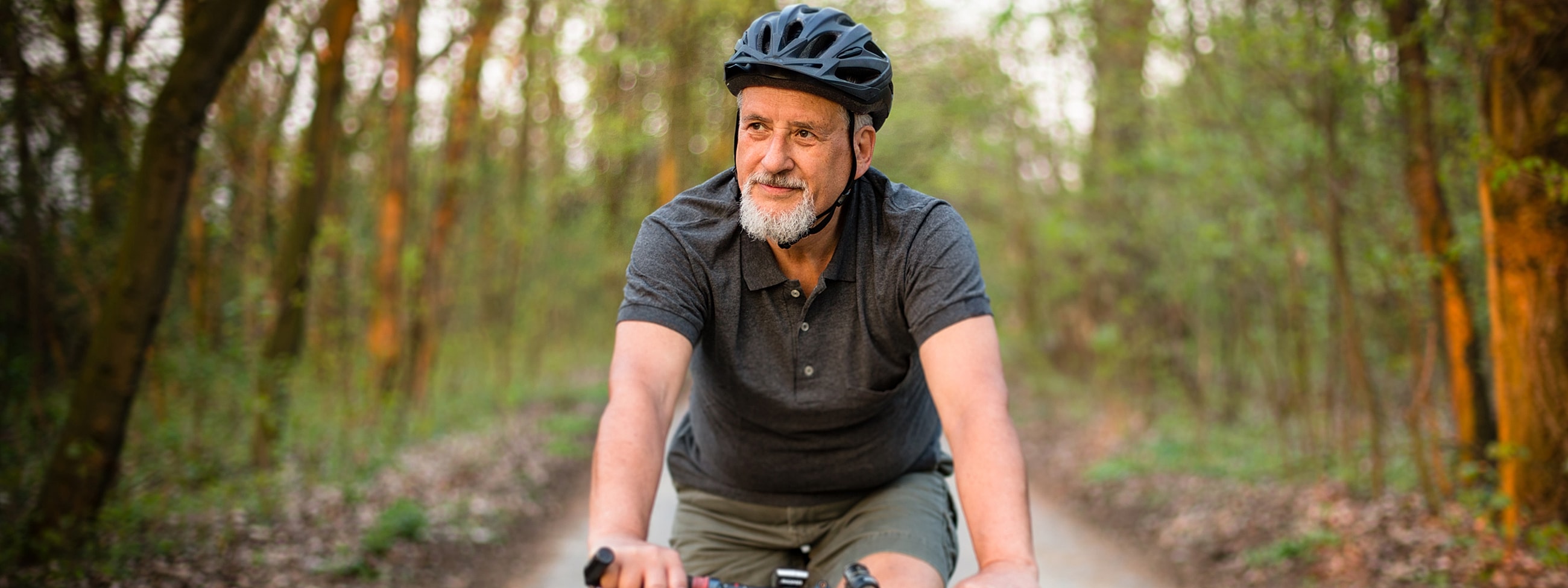 Senior man riding bicycle in forest trail.